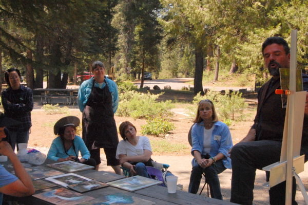 This is a photo of Stefan Baumann as he reviews participants' plein air paintings at the end of a Summer Workshop