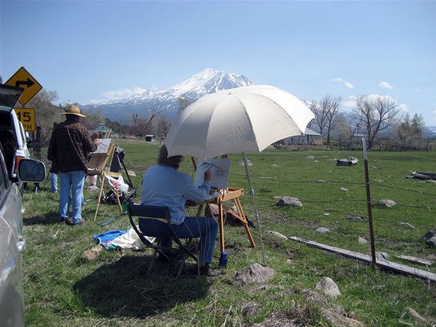 This photo is of a view of Mt. Shasta from Louis Road during Spring Workshop with an artist who is painting under a large white umbrella.
